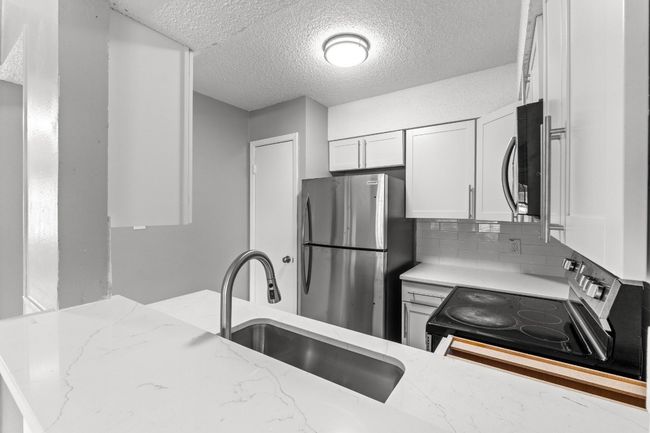 Kitchen with light stone counters, stainless steel appliances, a textured ceiling, and a sink | Image 13