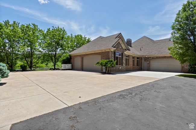 View of front of home with an attached garage, driveway, brick siding, a chimney, and roof with shingles | Image 76