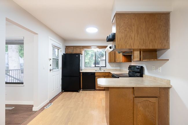 Kitchen with black appliances, light countertops, a peninsula, light wood finished floors, and brown cabinetry | Image 9