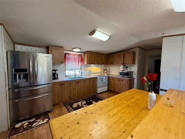 Kitchen featuring light wood finished floors, brown cabinetry, appliances with stainless steel finishes, vaulted ceiling, and a sink | Image 14
