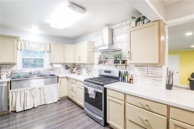 Kitchen featuring appliances with stainless steel finishes, wall chimney range hood, cream cabinetry, decorative backsplash, and recessed lighting | Image 4