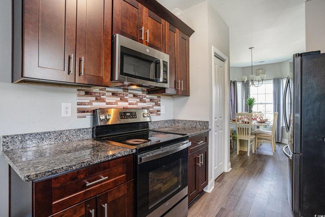 Kitchen with stainless steel appliances, a chandelier, wood finished floors, dark stone countertops, and hanging light fixtures | Image 8