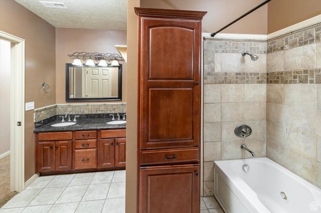 Bathroom with a textured ceiling, tiled shower / bath combo, vanity, and tile patterned floors | Image 38