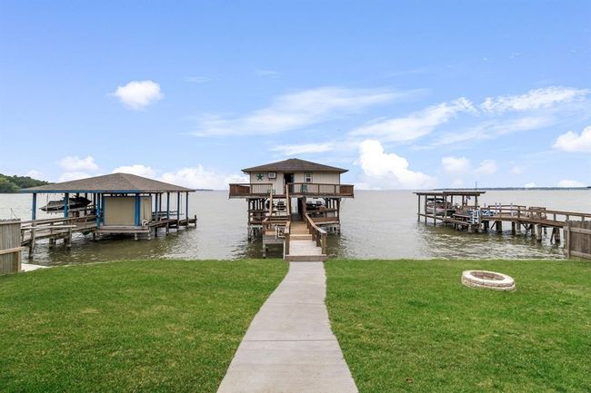 This photo showcases a lakeside property featuring a wooden dock leading to a boathouse, surrounded by calm waters. The setting includes a well-maintained grassy yard and a fire pit, ideal for outdoor activities and relaxation. | Image 32