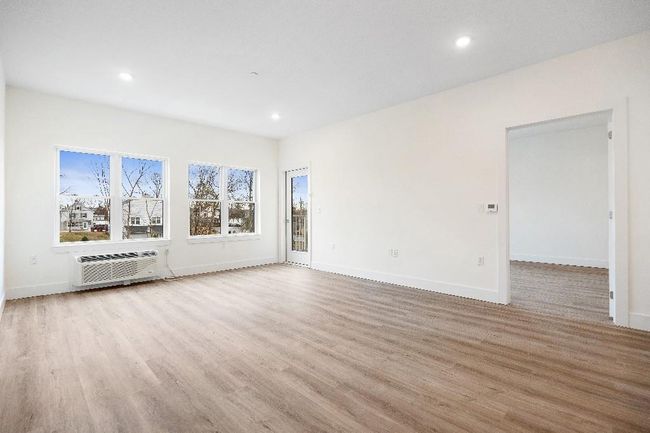 Unfurnished living room featuring a wall unit AC, light wood-style floors, recessed lighting, and baseboards | Image 12