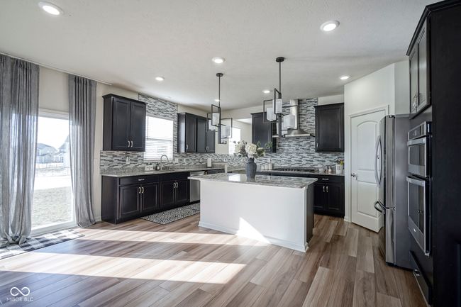 kitchen with light wood finished floors, a kitchen island, appliances with stainless steel finishes, light stone counters, and wall chimney range hood | Image 17