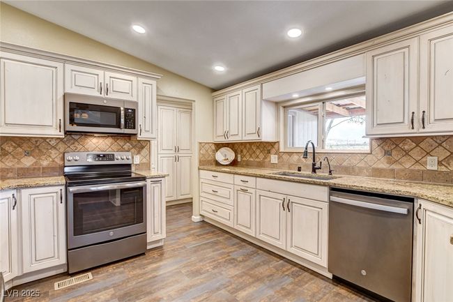 Kitchen with stainless steel appliances, vaulted ceiling, light wood-style flooring, tasteful backsplash, and light stone counters | Image 22