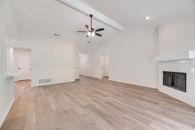 Unfurnished living room with a ceiling fan, a brick fireplace, beam ceiling, high vaulted ceiling, and light wood-style flooring | Image 6