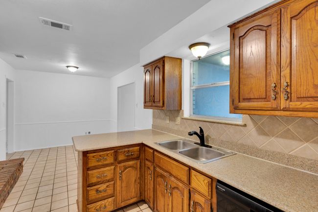 Kitchen with decorative backsplash, brown cabinetry, visible vents, a sink, and a peninsula | Image 15