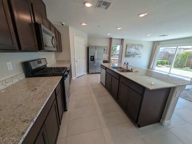 Kitchen featuring appliances with stainless steel finishes, plenty of natural light, a center island with sink, light tile patterned floors, and recessed lighting | Image 10