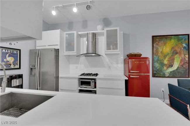 Kitchen with appliances with stainless steel finishes, wall chimney exhaust hood, white cabinetry, light countertops, and glass insert cabinets | Image 18