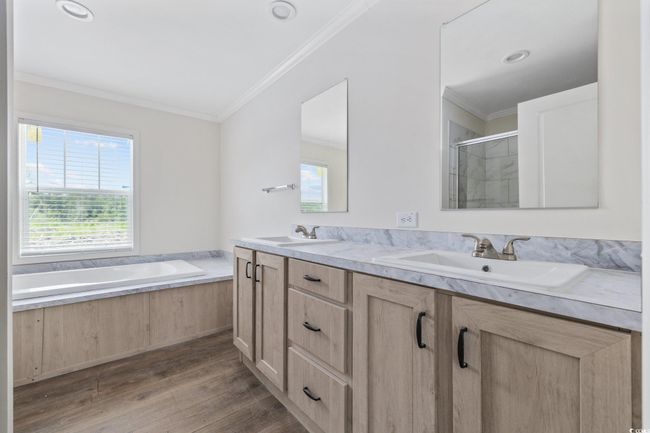 Bathroom with double vanity, wood finished floors, a stall shower, a bath, and crown molding | Image 27
