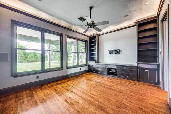 Unfurnished living room featuring wood finished floors, healthy amount of natural light, a ceiling fan, built in study area, and a textured ceiling | Image 12