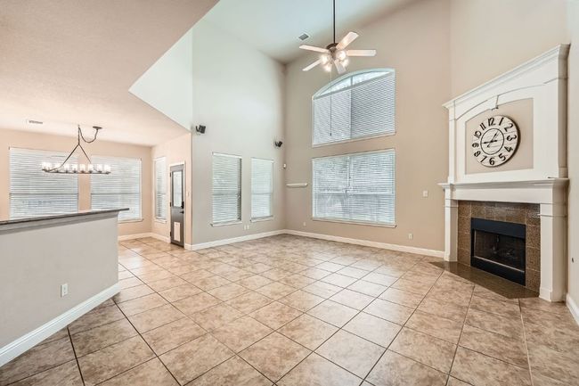 Unfurnished living room with a tiled fireplace, baseboards, ceiling fan with notable chandelier, and light tile patterned flooring | Image 7