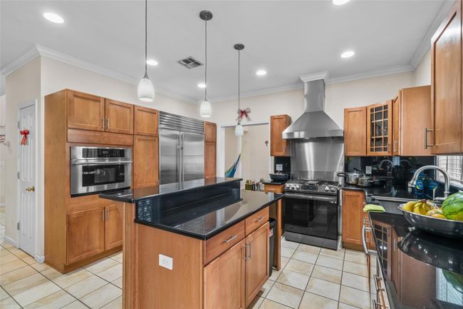 Kitchen with wall chimney range hood, visible vents, a kitchen island, appliances with stainless steel finishes, and decorative backsplash | Image 11