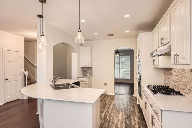 Kitchen with gas cooktop, arched walkways, backsplash, under cabinet range hood, and light countertops | Image 12