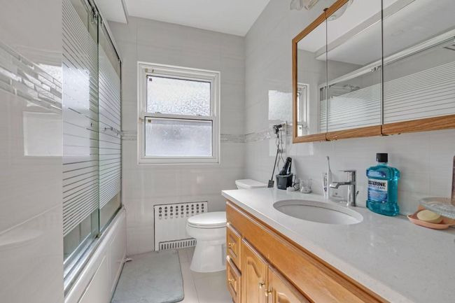 Bathroom featuring tile walls, radiator, vanity, bath / shower combo with glass door, and tile patterned flooring | Image 12