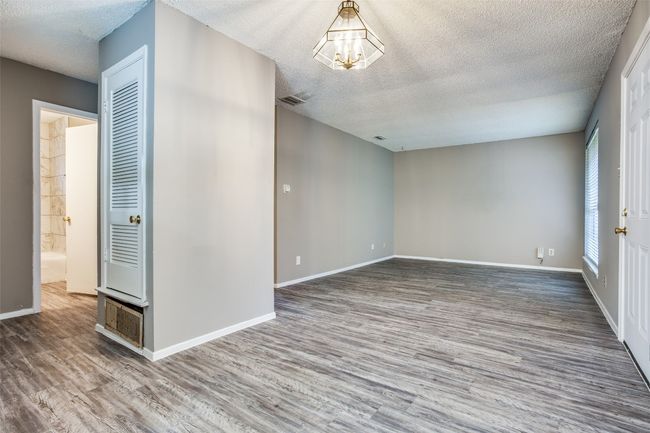 Empty room with a textured ceiling, a chandelier, wood finished floors, and visible vents | Image 4