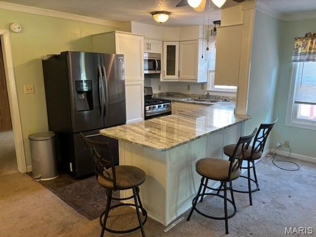 Kitchen featuring appliances with stainless steel finishes, dark carpet, a kitchen breakfast bar, crown molding, and a textured ceiling | Image 18