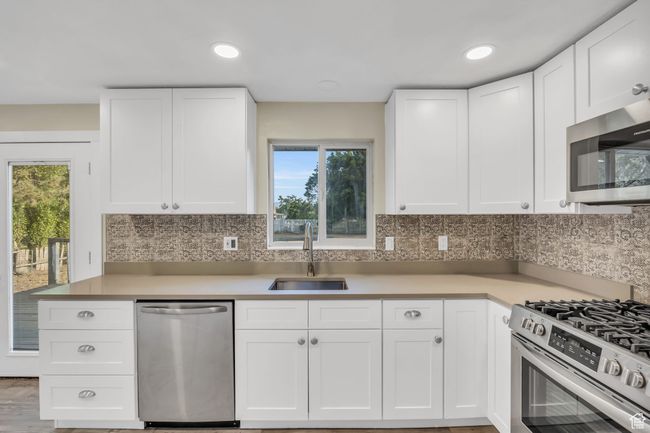 Kitchen with decorative backsplash, white cabinetry, a sink, and appliances with stainless steel finishes | Image 4