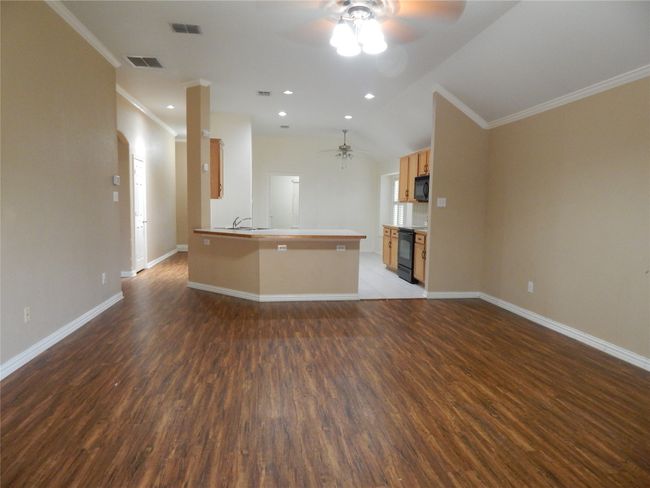 Unfurnished living room with a ceiling fan, wood finished floors, crown molding, and lofted ceiling | Image 5