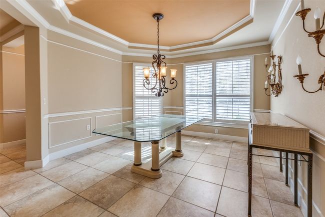 Dining room featuring a tray ceiling, crown molding, an inviting chandelier, a decorative wall, and wainscoting | Image 7
