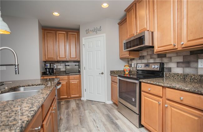 Kitchen featuring recessed lighting, light wood-style flooring, appliances with stainless steel finishes, a sink, and dark stone counters | Image 9