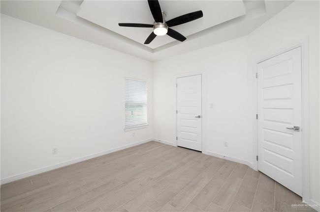Unfurnished bedroom with a tray ceiling, light wood-type flooring, and ceiling fan | Image 8