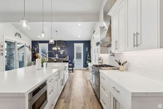 Kitchen featuring wall chimney range hood, white cabinets, a sink, stainless steel appliances, and recessed lighting | Image 39