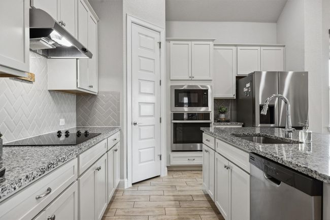 Kitchen featuring double oven, under cabinet range hood, appliances with stainless steel finishes, white cabinetry, and decorative backsplash | Image 5