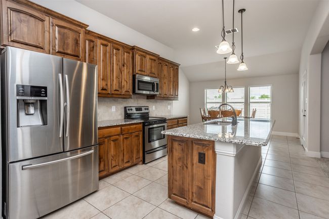 Kitchen featuring stainless steel appliances, light tile patterned floors, vaulted ceiling, tasteful backsplash, and a center island with sink | Image 17