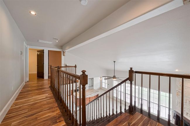 A bird’s-eye view from the upstairs landing highlights the two-story living area, showcasing wood-look floors and iron-spindled railing that adds classic architectural interest. | Image 47
