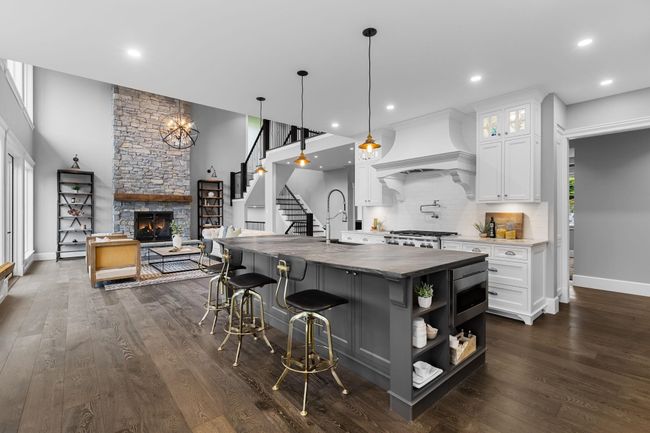 Kitchen featuring premium range hood, a stone fireplace, stove, decorative backsplash, and white cabinetry | Image 12