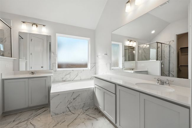 Full bath featuring lofted ceiling, a garden tub, a marble finish shower, two vanities, and marble look tile flooring | Image 22