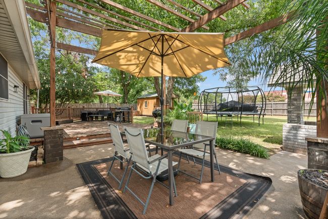 Fenced backyard featuring a trampoline, outdoor dining area, a storage unit, and a pergola | Image 22
