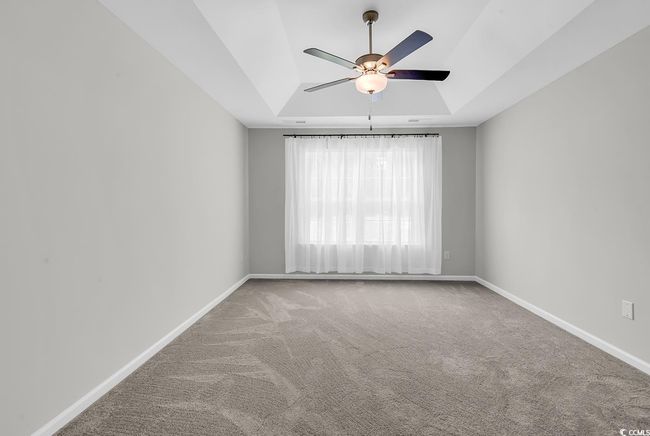 Carpeted empty room featuring a raised ceiling, ceiling fan, and baseboards | Image 24
