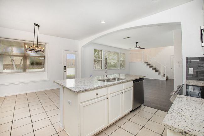 Kitchen featuring a sink, white cabinetry, light tile patterned floors, ceiling fan with notable chandelier, and stainless steel appliances | Image 13