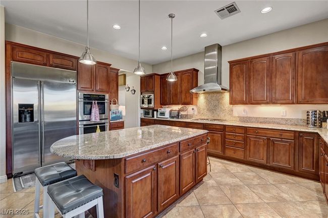 Kitchen featuring stainless steel appliances, wall chimney exhaust hood, a kitchen island, light stone counters, and light tile patterned floors | Image 19
