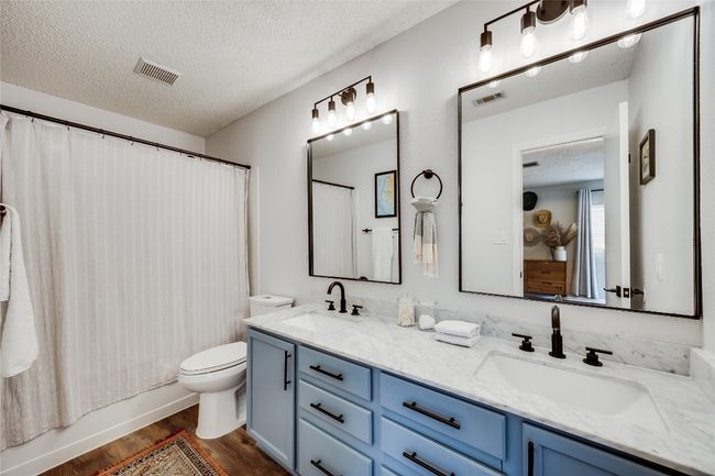 Bathroom featuring a textured ceiling, double vanity, toilet, wood finished floors, and shower / bath combo with shower curtain | Image 23