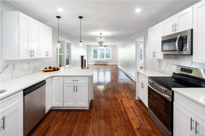 Kitchen with hanging light fixtures, kitchen peninsula, white cabinets, appliances with stainless steel finishes, and dark hardwood / wood-style flooring | Image 1