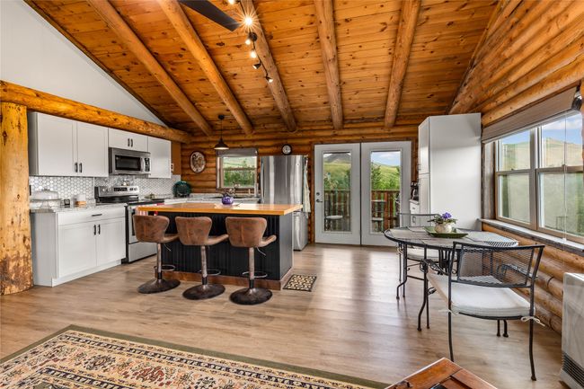 Kitchen with appliances with stainless steel finishes, a wooden ceiling with exposed beams, rustic walls, white cabinetry, and wood counters | Image 7