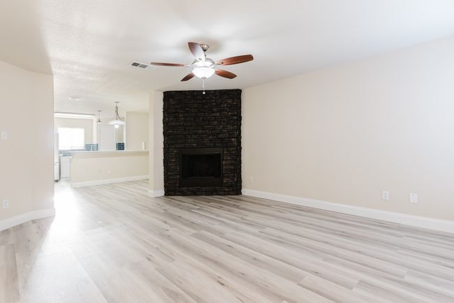 Unfurnished living room featuring visible vents, baseboards, a ceiling fan, light wood-type flooring, and a brick fireplace | Image 4