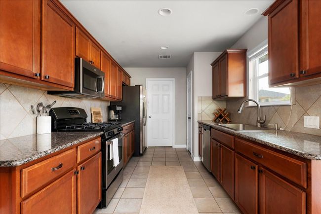 Kitchen featuring stainless steel appliances, a sink, tasteful backsplash, baseboards, and light tile patterned floors | Image 7