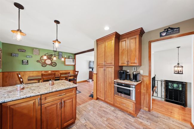 Kitchen with light stone countertops, brown cabinets, light wood-type flooring, decorative light fixtures, and wall oven | Image 12