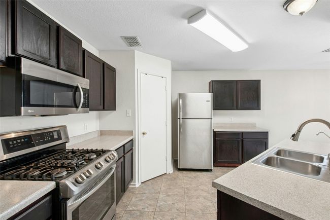 Kitchen with stainless steel appliances, light countertops, and dark brown cabinetry | Image 9