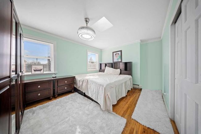 Bedroom with wood finished floors, a skylight, a closet, a baseboard heating unit, and crown molding | Image 16