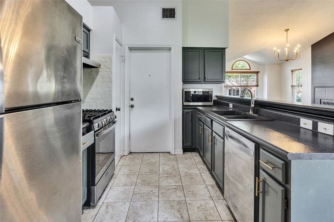 Kitchen featuring appliances with stainless steel finishes, dark countertops, vaulted ceiling, a peninsula, and light tile patterned floors | Image 6