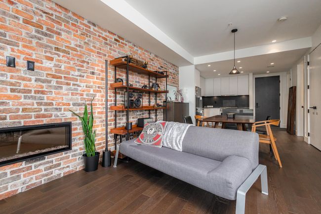 Living area with wood finished floors, a fireplace, and brick wall | Image 10