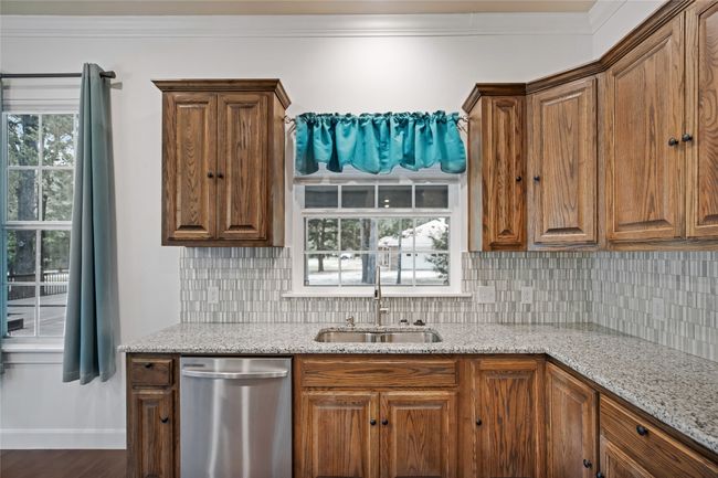 Kitchen with dishwasher, decorative backsplash, light stone countertops, ornamental molding, and brown cabinetry | Image 12