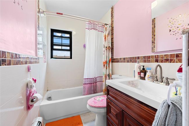 Full bathroom with toilet, tile walls, vanity, shower / tub combo with curtain, and baseboard heating | Image 10